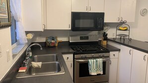 Eine Küche mit Spüle aus Edelstahl, einer Mikrowelle, einem Backofen und einer Uhr an der Wand.