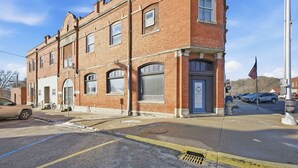 A two-story brick building with a blue door, a garage door, and a small American flag. - Cozy 1-bedroom apartment in peaceful Wathena with AC (Wathena)
