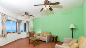 Ein Wohnzimmer mit Sofa, Couchtisch, Lampe, Deckenventilator und Blick durch das Fenster.