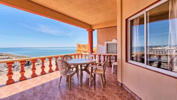 Ein Balkon mit Tisch und Stühlen, Blick aufs Meer und ein Gebäude im Hintergrund.