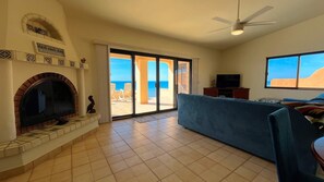 A living room with a fireplace, a television, and a view of the beach. - Charming 3-Bedroom Beachfront Home Bahia Delfin (Las Conchas)