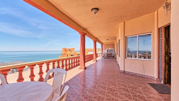Balcón techado con vistas al mar, una mesa y sillas, y una puerta con ventanal.