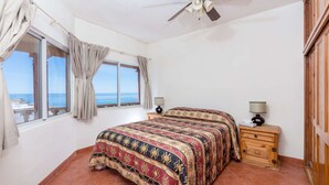 Un dormitorio con cama, dos mesitas de noche, ventilador de techo y vista al mar.