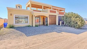 A modern two-story house with a covered patio, a garage, and a gravel driveway. - Cozy, Quiet & Beautiful Home Borracho Flat (Bahía la Choya)