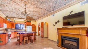 A kitchen with a stone ceiling, wooden cabinets, a central island, a fireplace, and a television mounted on the wall. - Cozy, Quiet & Beautiful Home Borracho Flat (Bahía la Choya)