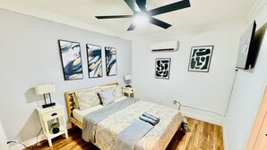 Ein Schlafzimmer mit Bett, Nachttisch, Deckenventilator und Wandbildern.