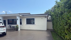Einbungalow mit befestigter Auffahrt, weißer Fassade und kleiner Terrasse mit Tisch und Stühlen.