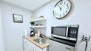 Eine kleine Küche mit einer Mikrowelle, einem Spülbecken und einer Wanduhr.