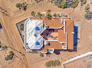 Eine Vogelperspektive eines Hauses mit einer großen, zentralen Terrasse, mehreren Zimmern und einem markanten Dachdesign.