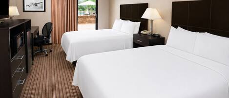 A hotel room with two beds, a desk with a chair, a TV, and a view of an outdoor area.