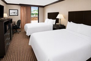 A hotel room with two beds, a desk with a chair, a TV, and a view of an outdoor area. - Baymont By Wyndham Schaumburg Chicago Northwest (Schaumburg)