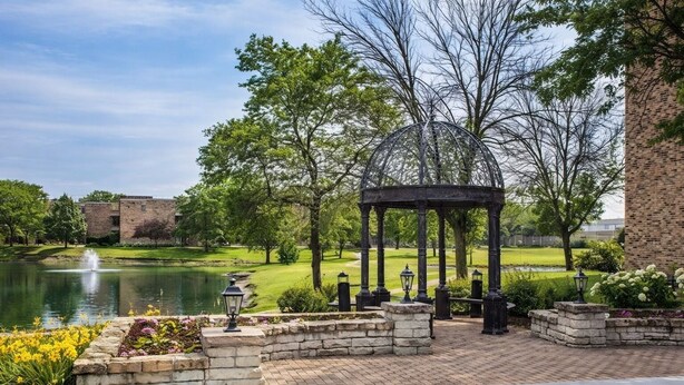 A gazebo with a brick wall, a pond, and a building in the background. - Baymont By Wyndham Schaumburg Chicago Northwest (Schaumburg)