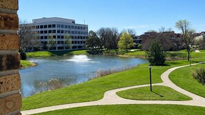A park with a pond, a walking path, and a building in the background. - Baymont By Wyndham Schaumburg Chicago Northwest (Schaumburg)