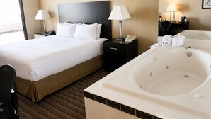 A hotel room with a large bed, two bedside tables with lamps, a black headboard, a large bathtub, and a window. - Baymont By Wyndham Schaumburg Chicago Northwest (Schaumburg)