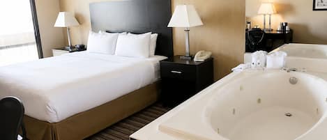 A hotel room with a large bed, two bedside tables with lamps, a black headboard, a large bathtub, and a window.