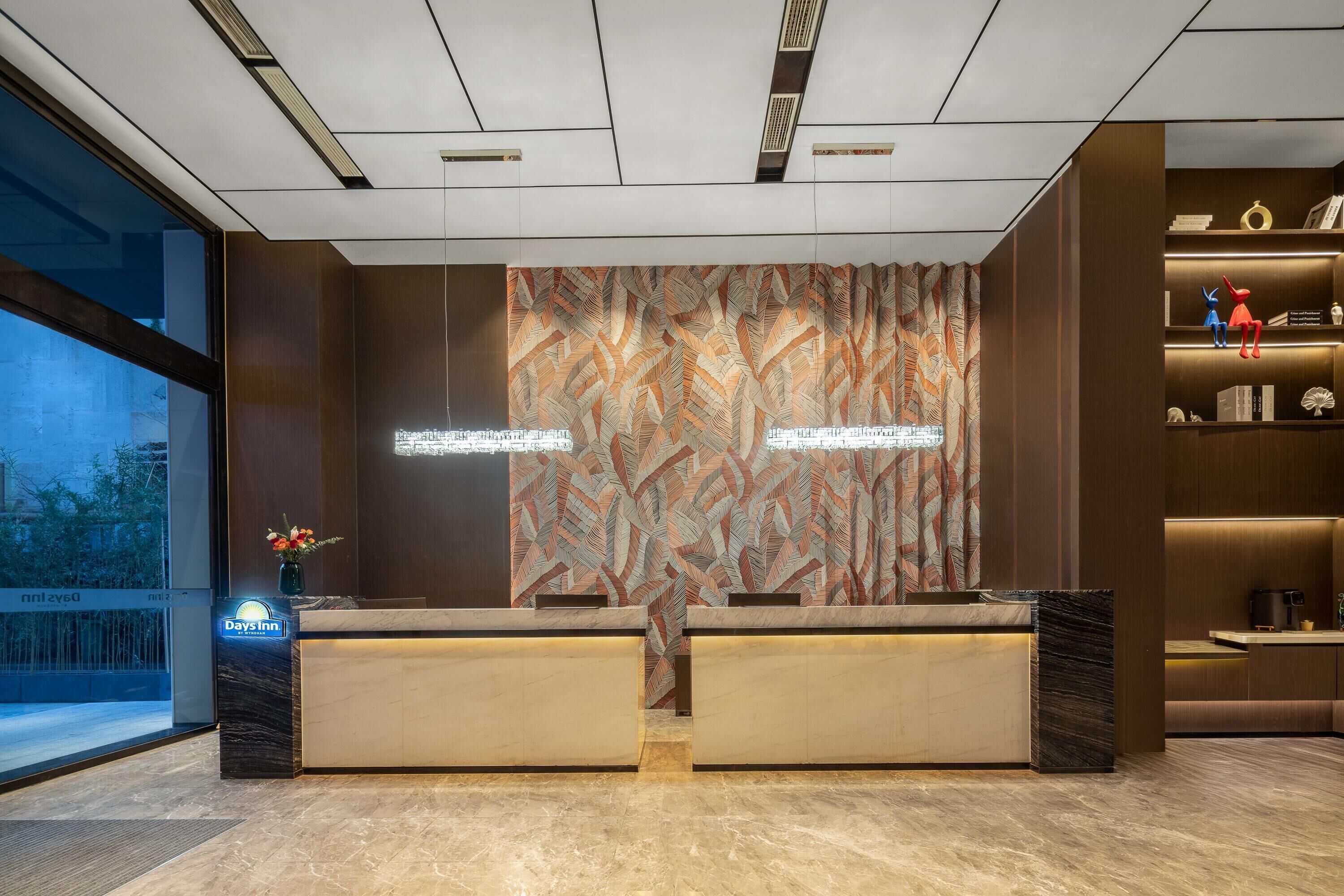 Un'area reception di un hotel dal design moderno, con una scrivania della reception, una parete decorata e vista sull'esterno.