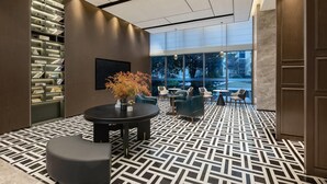A modern lobby with a patterned floor, a round table with a vase, and a bookshelf.