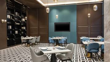 A modern dining area with tables, chairs, a TV screen, and a wine rack.