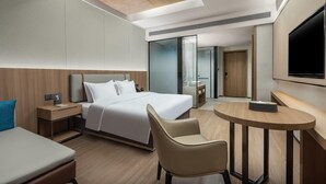 A modern hotel room with a bed, bedside table, chair, and a small round table.