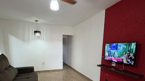 A living room with a sofa, a ceiling fan, a television mounted on a red wall, and a tiled floor. - Agrishow house, sleeps 4 / 2 bedrooms / 1 bathroom (Ribeirão Preto)
