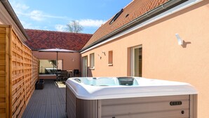 Ein Whirlpool auf einer Holzdiele, ein Holzzaun und ein Gebäude mit einem Ziegeldach.