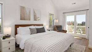 Ein Schlafzimmer mit einem großen Bett, einem Nachttisch, einem Sessel und einem Balkon mit Blick.