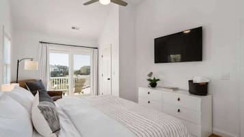 A bedroom with a bed, a ceiling fan, a TV mounted on the wall, and a window with curtains.