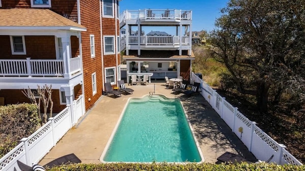 Ein zweistöckiges Haus mit Schwimmbad, Balkon und Gartenmöbeln.