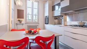 A modern kitchen with white cabinets, a gas stove, and a dining area with a table and red chairs. - Chica's Luxury Loft in the Heart of Lucca's Historic Center (Lucca)