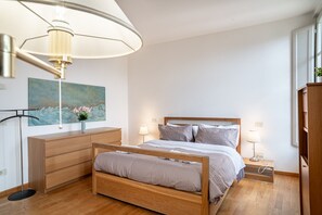 A bedroom with a wooden bed, bedside lamps, a nightstand, a desk with drawers, a floor lamp, and a painting on the wall. - Chica's Luxury Loft in the Heart of Lucca's Historic Center (Lucca)