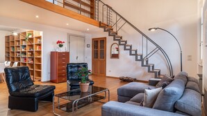 A spacious living area with a staircase, leather sofas, a glass coffee table, and a bookshelf. - Chica's Luxury Loft in the Heart of Lucca's Historic Center (Lucca)