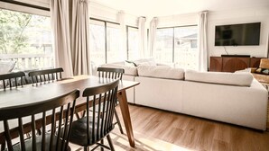 A room with a dining table, chairs, a sofa, a TV, and large windows. - Abbey Springs Resort with Golf Cart, Shared Pools (Fontana-on-Geneva Lake)