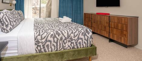 A bedroom with a bed, a TV, a wooden dresser, and a sliding glass door.