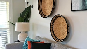 En stue med en grå sofa, dekorativ vægkunst i flet, en lampe og en potteplante.