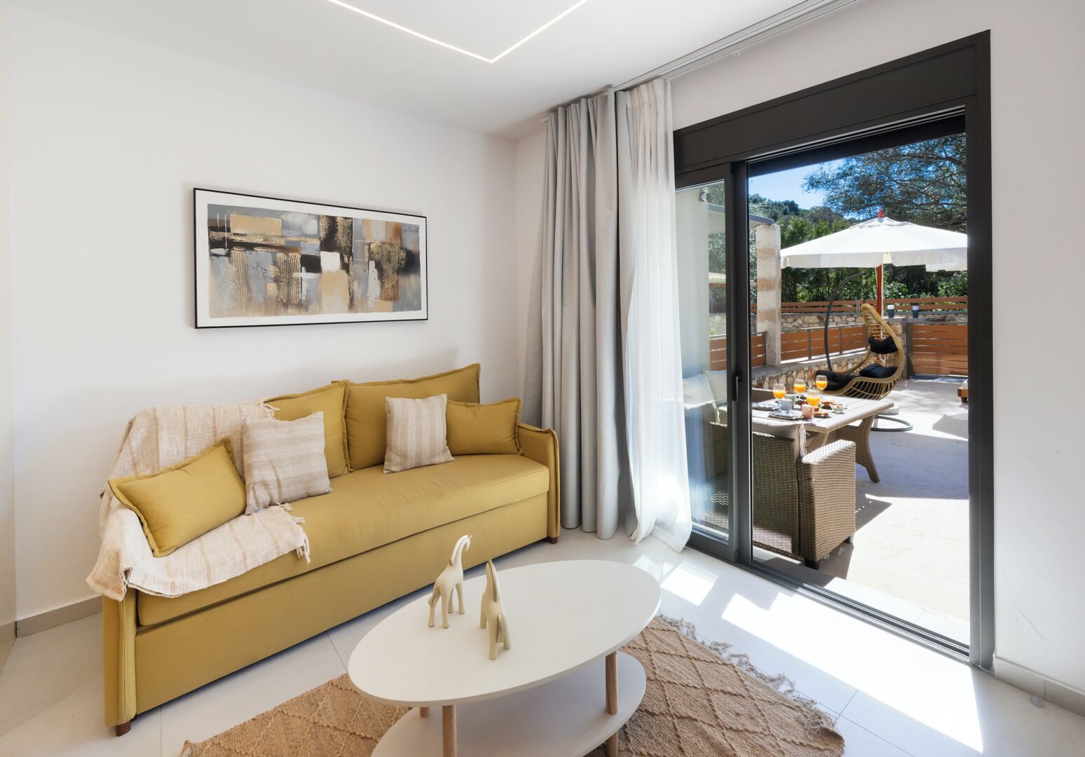 A modern living room with a sofa, a coffee table, and a large window with a view of an outdoor patio.