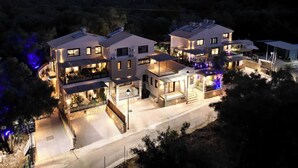 A modern multi-story hotel with a central courtyard, multiple balconies, and a well-lit exterior. - Nicole Collection - Meganisi Cove Suites (Meganisi)