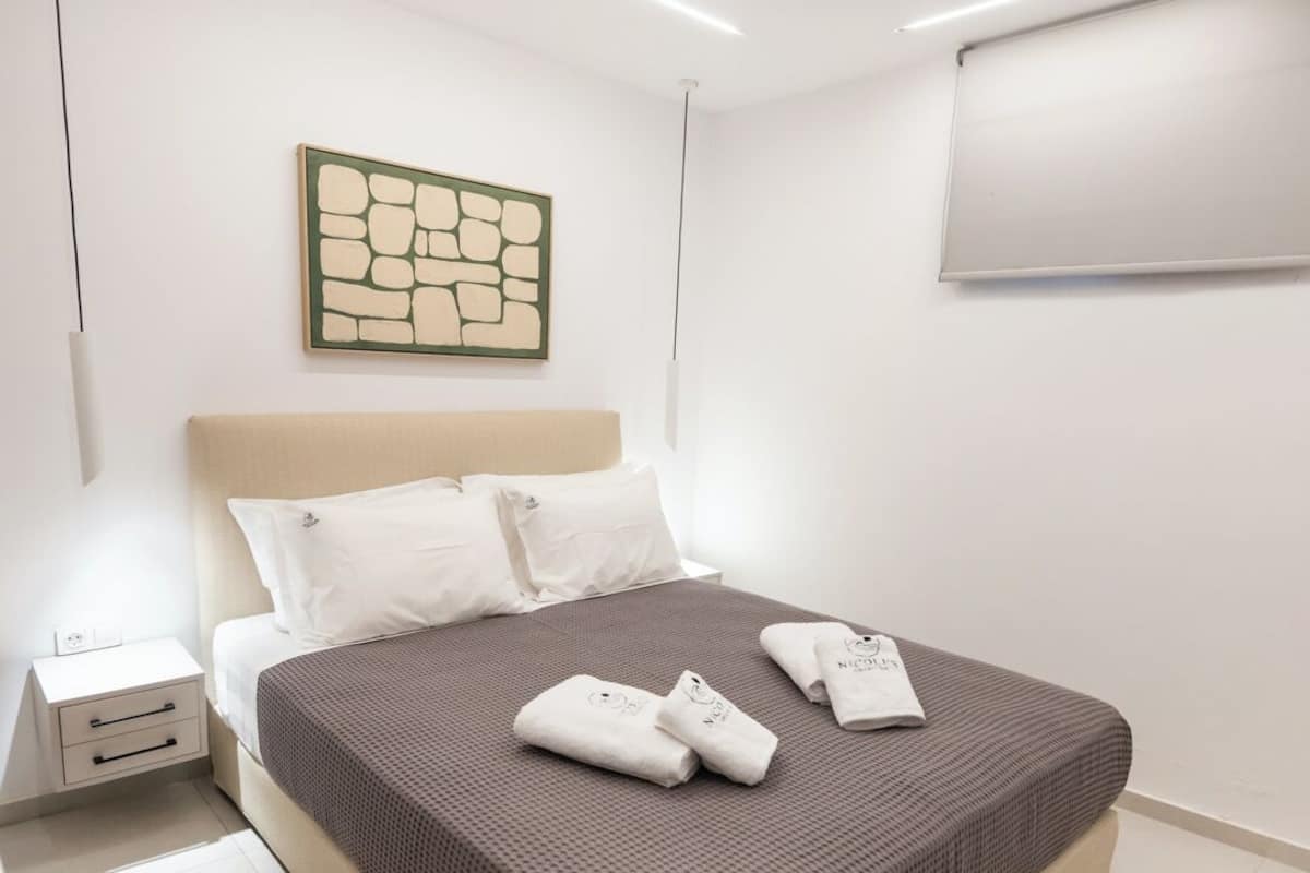 Une chambre à coucher moderne, avec un lit, des tables de chevet, une œuvre d’art accrochée au mur et un luminaire au plafond.