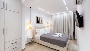 A modern bedroom with a bed, bedside tables, a wardrobe, and a TV mounted on the wall. - Nicole Collection - Meganisi Cove Suites (Meganisi)