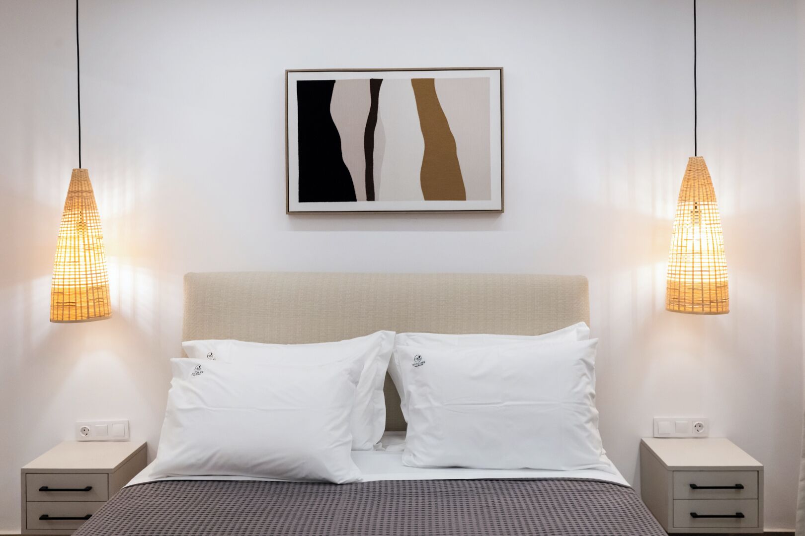 A neatly made bed with white pillows, a beige headboard, and two bedside tables with lamps.