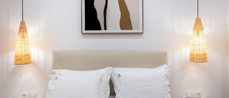 A neatly made bed with white pillows, a beige headboard, and two bedside tables with lamps.