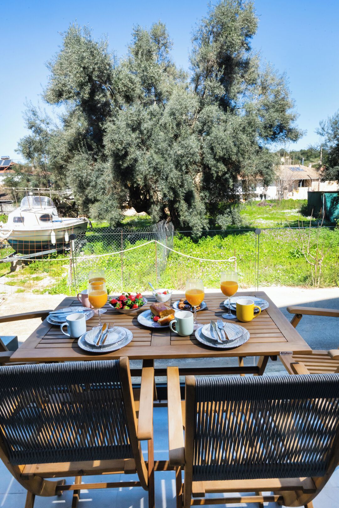 Mesa al aire libre con platos, vasos y cubiertos, rodeada de sillas.