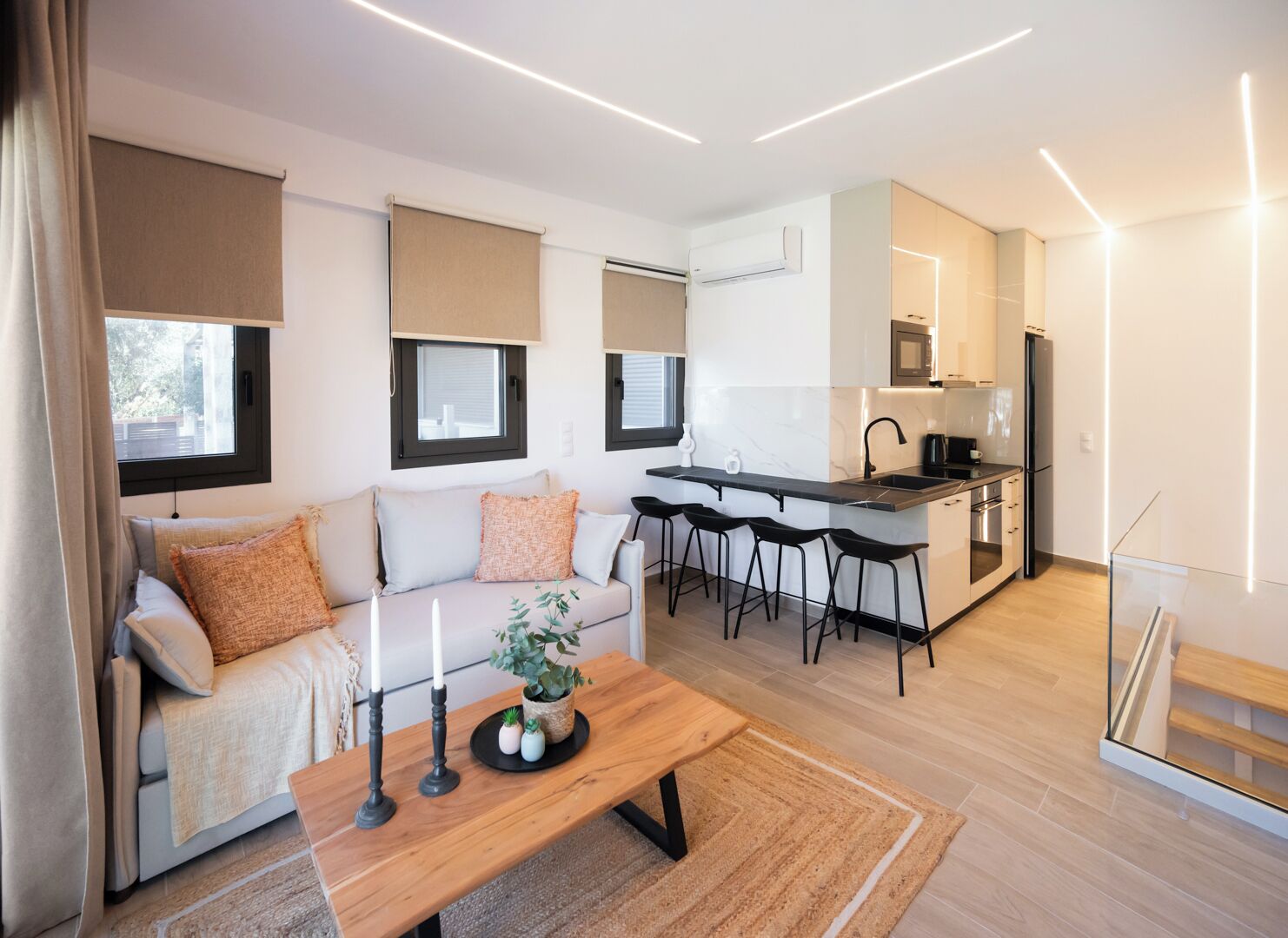 A modern living room with a sofa, a coffee table, and a kitchen area with a bar and stools.
