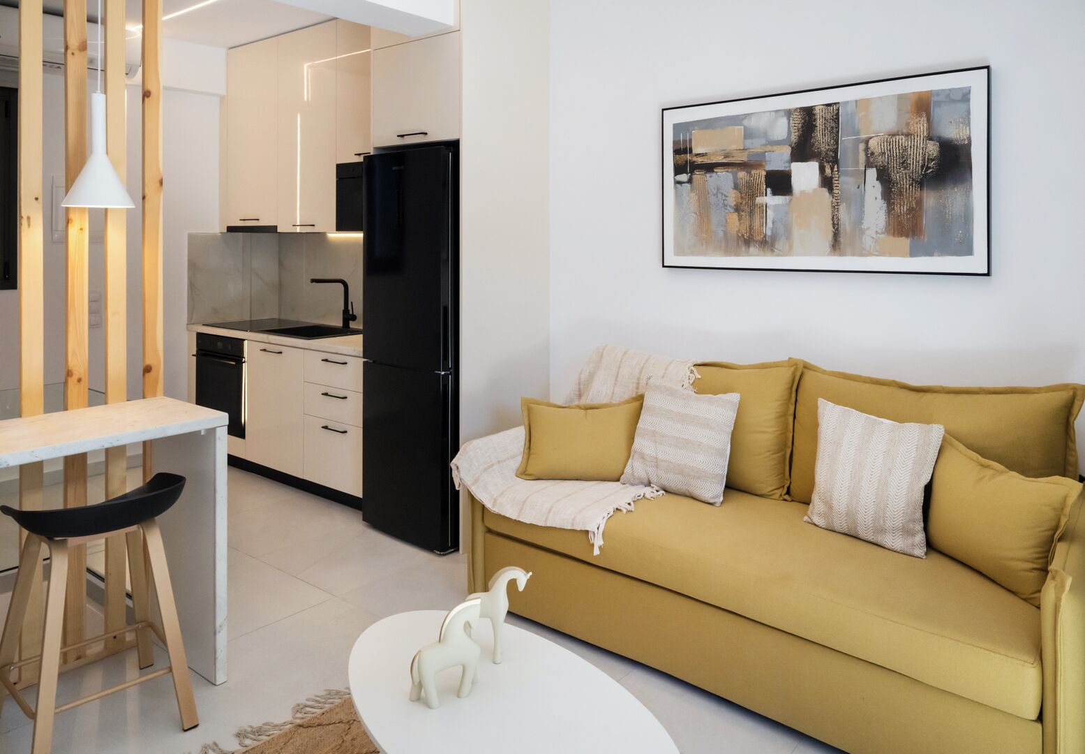 Una cocina moderna con un refrigerador negro, una mesa de comedor con sillas, un sofá con cojines y un cuadro abstracto enmarcado en la pared.