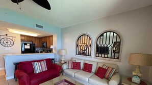 Una sala de estar con un sofá rojo, un sofá color beige, una mesa de centro y una cocina al fondo.