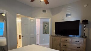 Un dormitorio con cama, televisor sobre un mueble de madera y puerta que da a otra habitación.