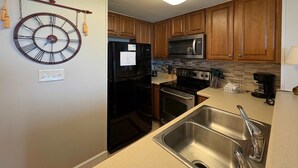 Una cocina con armarios de madera, un refrigerador negro, un microondas, una estufa y un lavamanos doble.