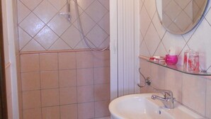 A bathroom with a shower, a sink, and a mirror. - Cozy studio apartment in rural house with garden 5 km from the sea (Ogliastro Cilento)