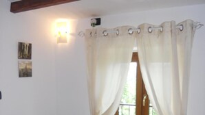 A room with a wooden door, white curtains, a small table with a sign, and a wall-mounted light fixture. - Cozy studio apartment in rural house with garden 5 km from the sea (Ogliastro Cilento)