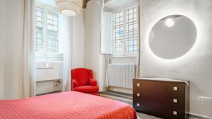 Een slaapkamer met een bed, een rode stoel, een kaptafel, een ronde spiegel en een raam met uitzicht.