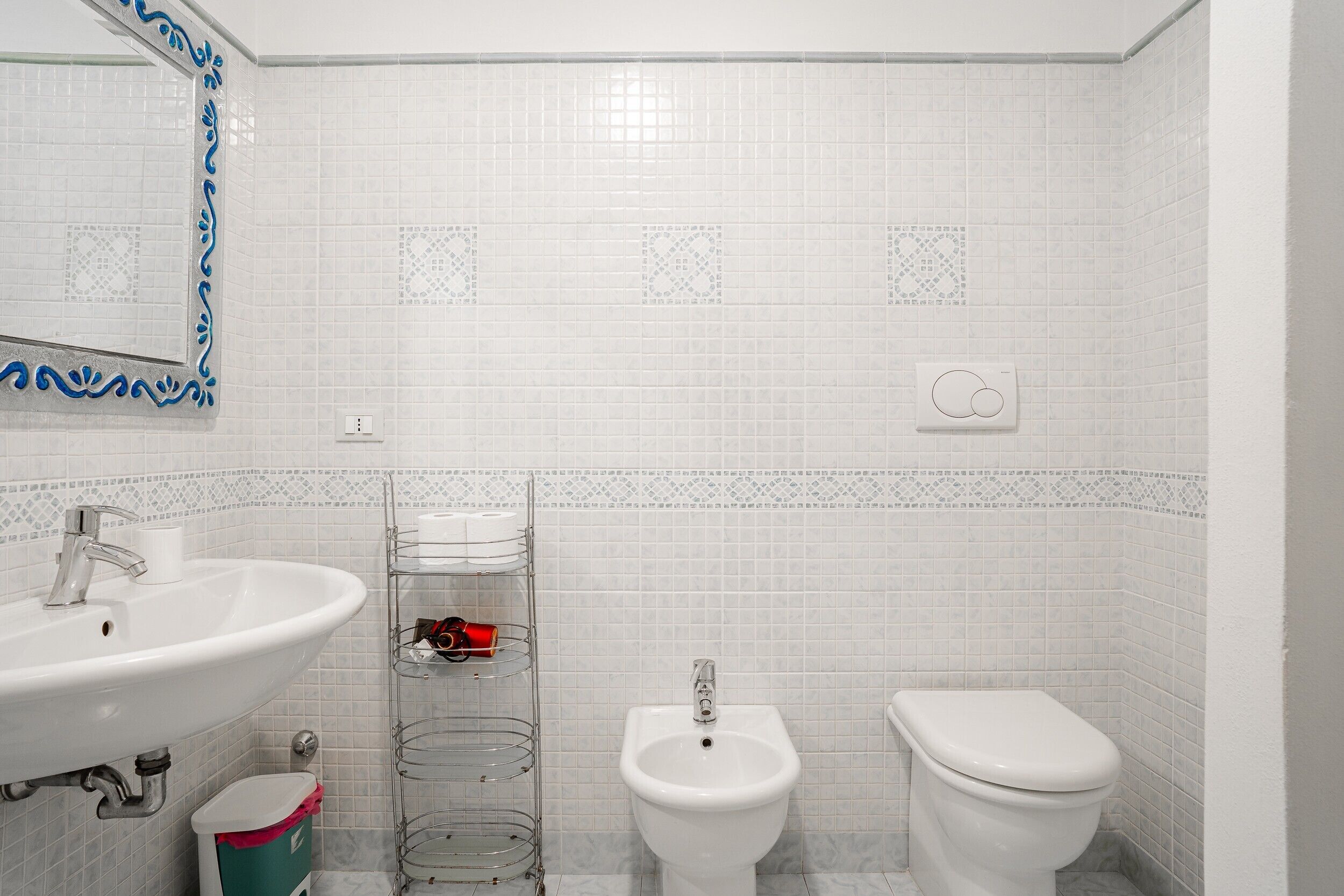 Un baño con lavamanos, bidé, inodoro y espejo con marco decorativo.
